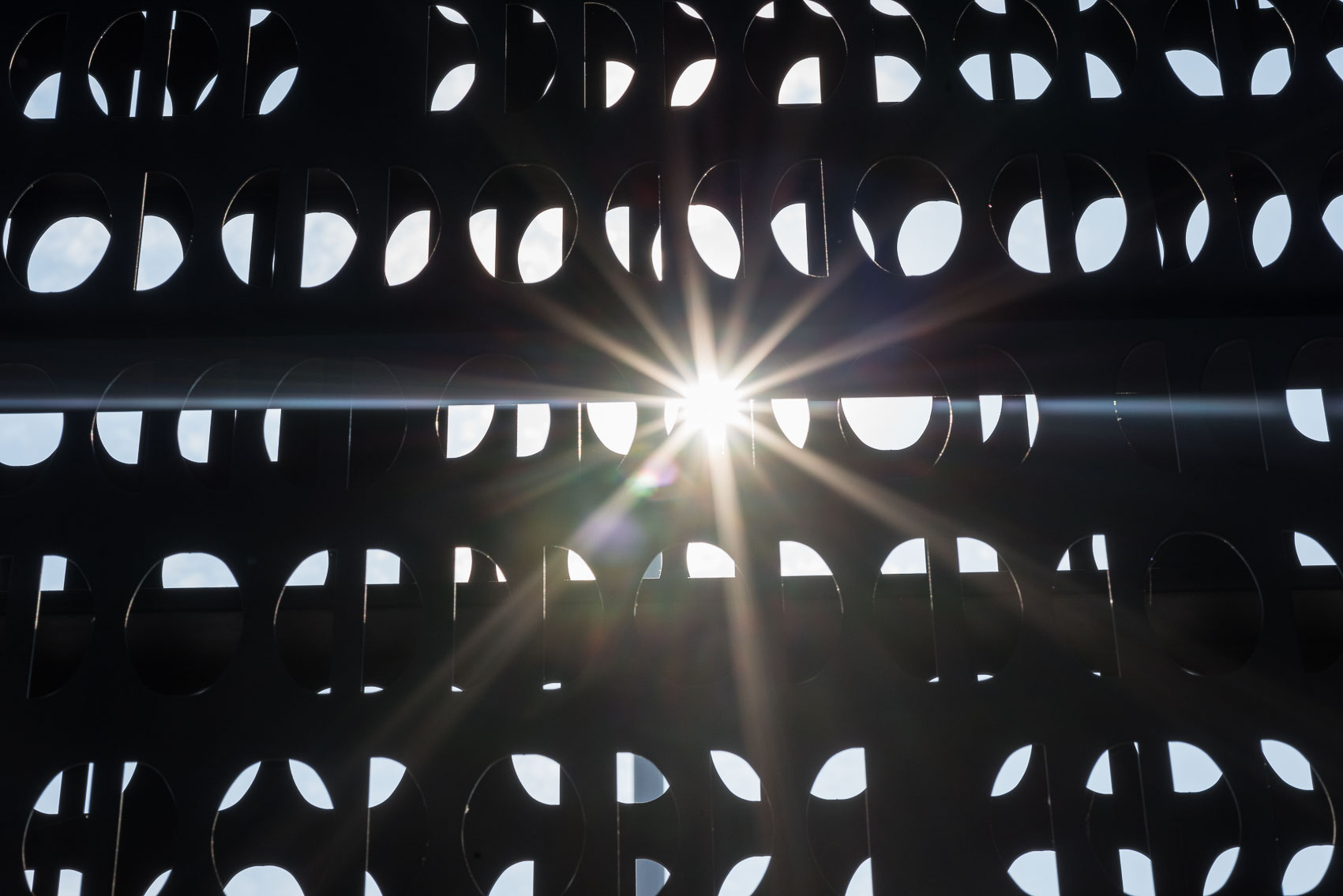 Sonnenstrahlen scheinen durch ein perforiertes Metallgitter und erzeugen ein faszinierendes Lichtspiel.