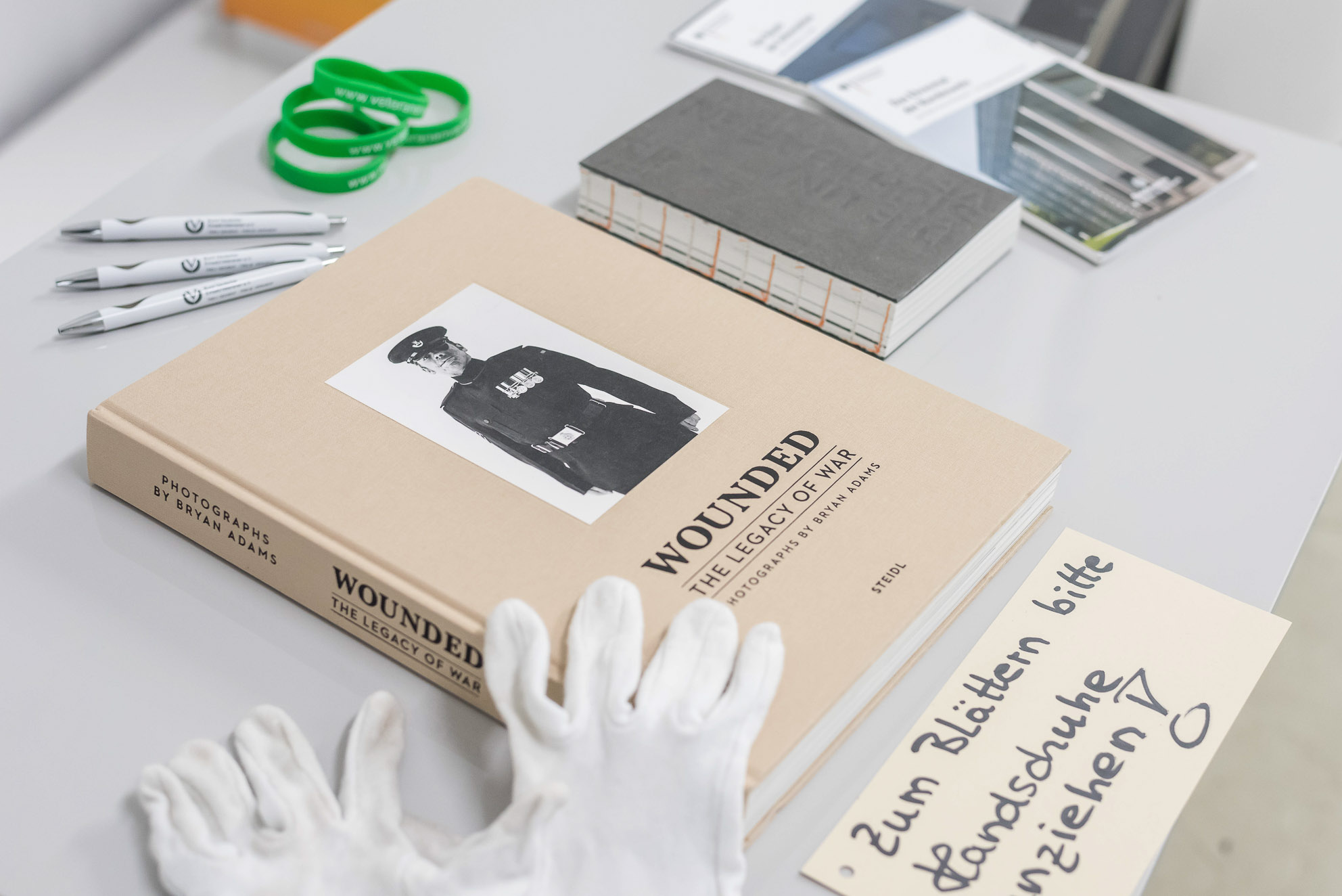 Auf einem Tisch liegen das Buch "Wounded", Stifte, Armbänder und Handschuhe mit einem Hinweis zum Blättern.