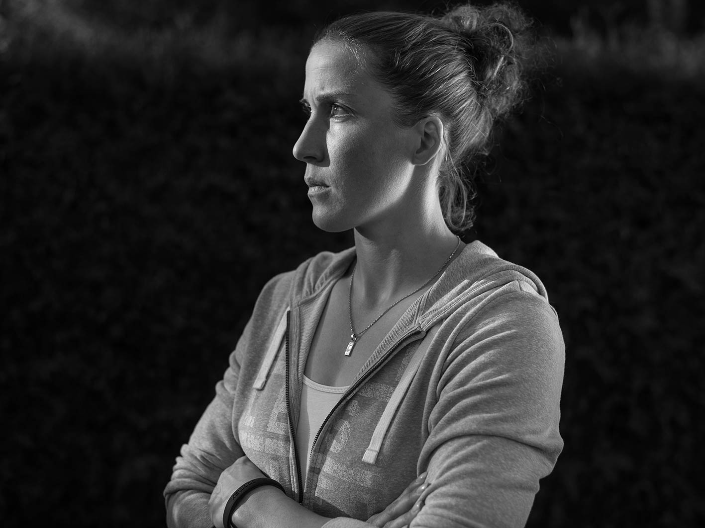 Eine nachdenkliche Frau in einem grauen Hoodie, die in Schwarz-Weiß aufgenommen wurde, steht mit verschränkten Armen.