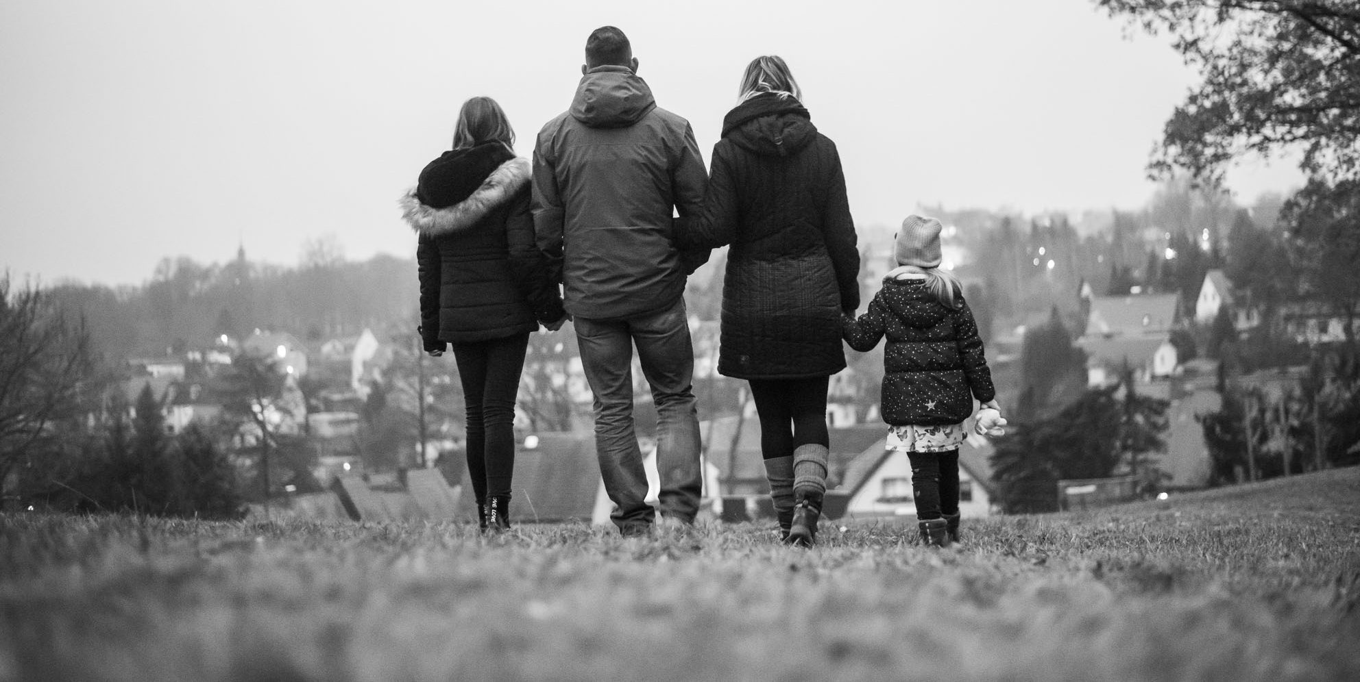 Eine Familie mit zwei Erwachsenen und zwei Kindern spaziert Hand in Hand auf einem Hügel mit Blick auf eine Stadt.