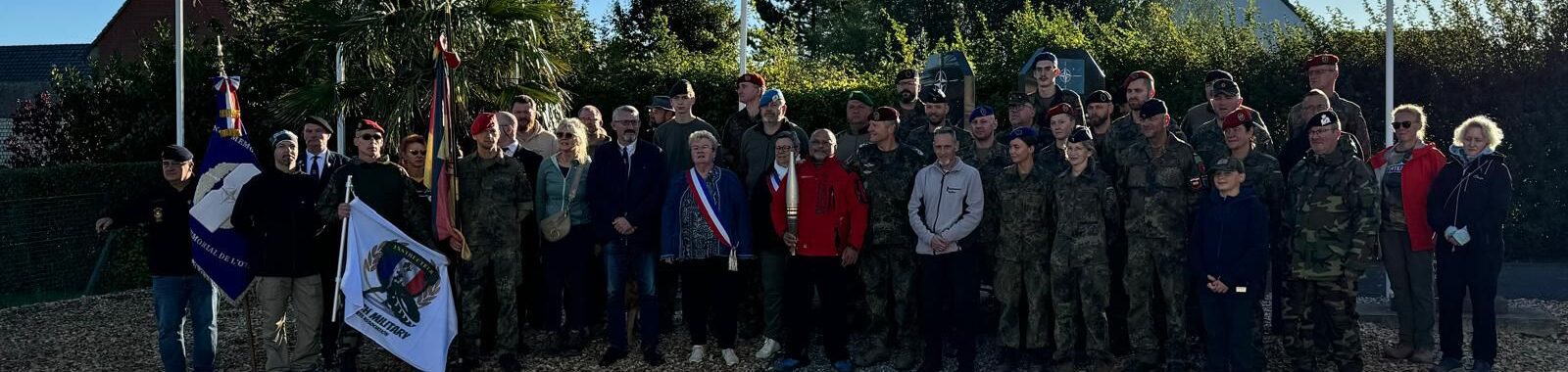 Gruppenfoto von Soldaten, Veteranen und Bürgern bei einer Gedenkveranstaltung mit Flaggen und Uniformen.